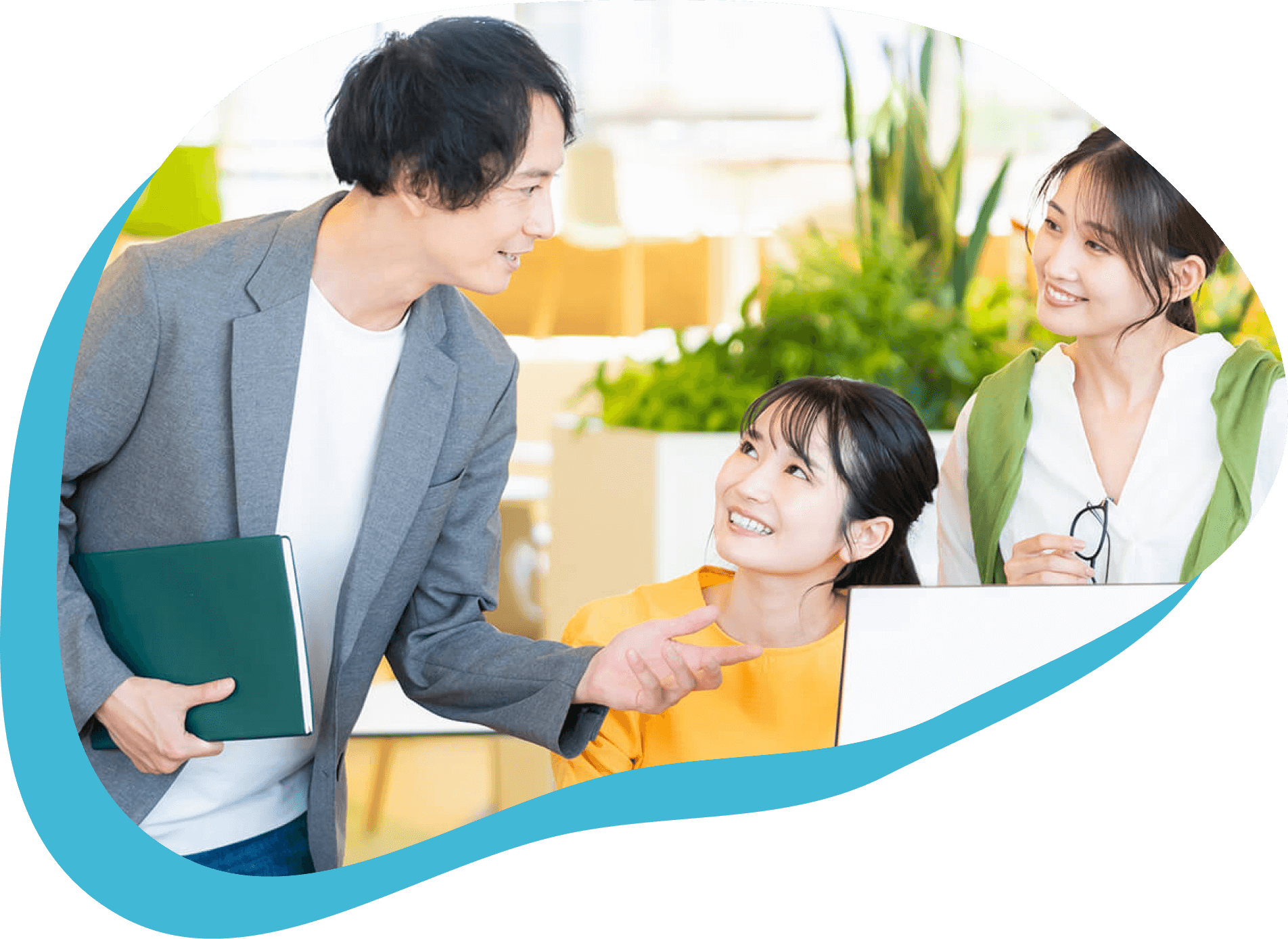 明るいオフィスで、三人の若い社会人がノートパソコンを囲み、笑顔で打ち合わせをしています。青い装飾が特徴的な企業